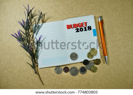 A pen, coins, a leaf and a notebook with a words BUDGET 2018 on a brown background. Conceptual image for new year 2018, business and finance.