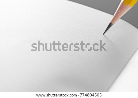 Minimalist close up photo of wooden yellow pencil target to write on curved white paper of notebook with copy space. Flash light made to show paper surface and long smooth shadow from yellow pencil.
