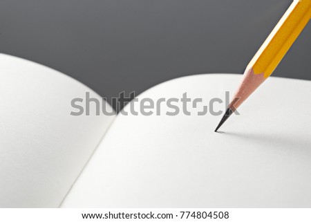 Minimalist close up photo of wooden yellow pencil target to write on curved white paper of notebook with copy space. Flash light made to show paper surface and long smooth shadow from yellow pencil.