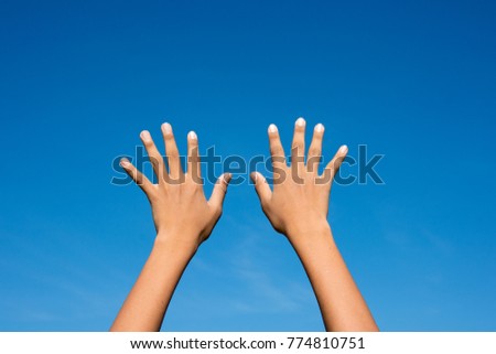 Two hands up in the air over blue sky background.