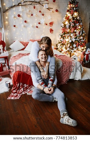 Pretty couple is hugging on by the sofa with Christmas presents in the boxes