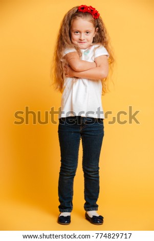 Photo of little funny girl child standing isolated over yellow background with arms crossed. Looking camera.