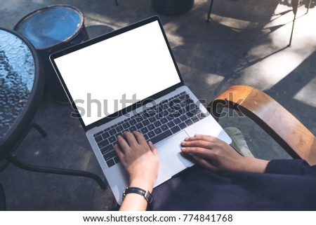 Mockup image of business woman using and typing on laptop with blank white screen , sitting on wooden chair in cafe