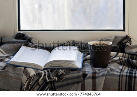 Cup, book, grey plaid on the window sill. Close up