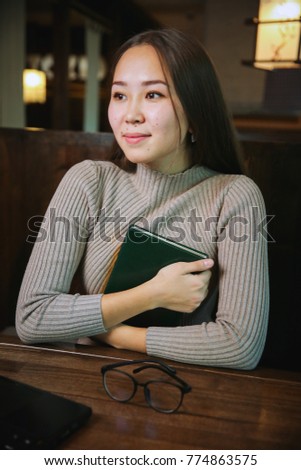 Beautiful woman in jacket of gray resting in a cozy cafe making notes in diary 
attractive young Manager of the planning of the work schedule with Notepad and Nobile phone is sitting at the table