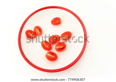Eight halves of red cherry tomatoes on white plate with red border on white. Minimalistic style. Above view
