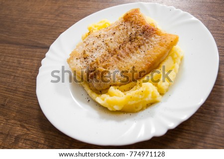 Fried fish fillet of cod with mashed potato in white plate on wooden background.