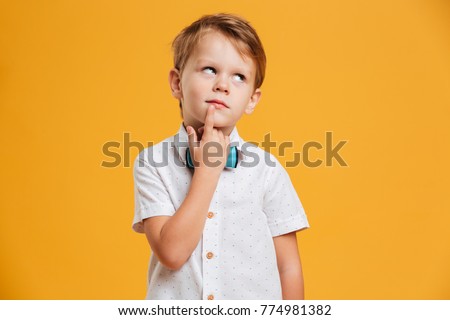 Picture of thinking little boy child standing isolated over yellow background. Looking aside.