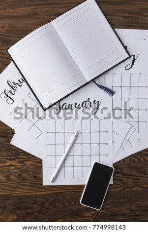 flat lay with empty notebook, calendar, pencil and smartphone on wooden surface