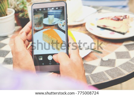 Woman's hand taking photo of sweet orange cake on mobile phone while sitting in cafe, female looking and using cellphone during breaking and relaxing time 