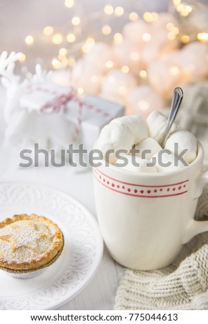 White Mug with Hot Chocolate Cocoa Drink and Marshmallows on Top Mince Pie on Plate. Sparkling Garland Lights in Background. Knitted Sweater Gift Box Christmas New Year Advent Morning Cozy