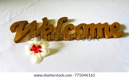 Welcome sign and a plumeria flower on white linin tablr cloth