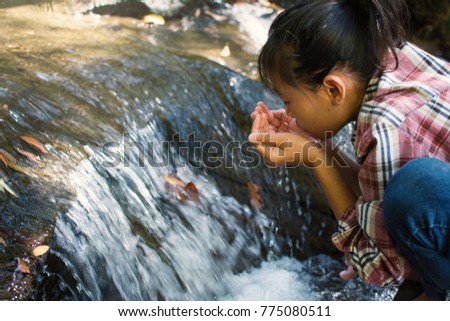 Cute girl drinking water from waterfall stream on forest