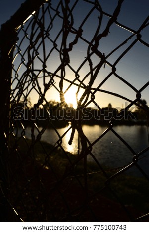sunset/sunrise piercing through fence with reflection off lack. warm blue sky  and water