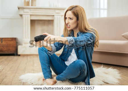 Having fun. Beautiful determined blond young woman smiling and playing a game while sitting on the carpet on the floor and wearing a jeans costume