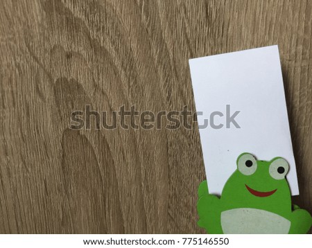 Cute white card and cute frog cartoon with brown wooden table background.