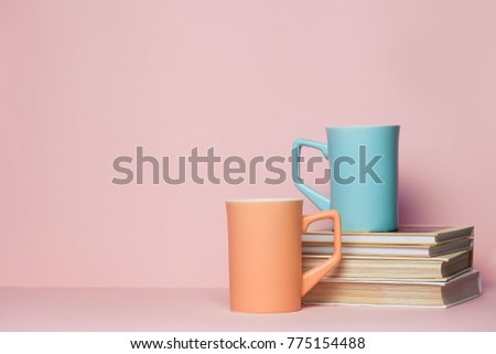 Close up of two cups and a book on pink background. Copy space for your text or design.