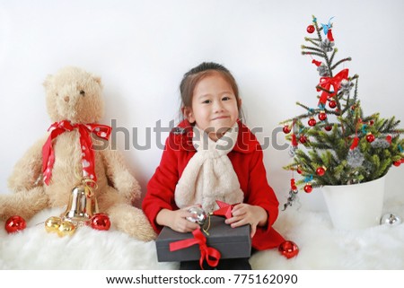 kid girl dressed as Santa Claus sitting near Christmas tree with holding gift on white background.