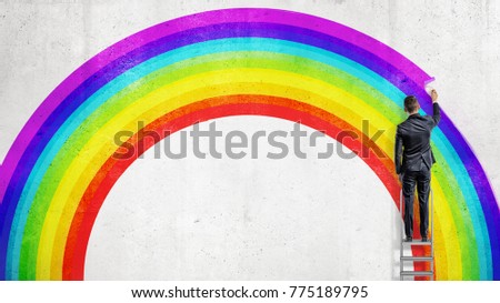 A businessman stands on a stepladder and drawing the last colorful line in the wall picture of a rainbow. Business and dreams. Uncommon and unusual plans. Different and unique vision.