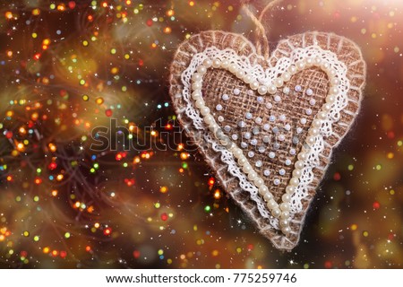 Merry Christmas handmade sackcloth toy heart. blurred background with garland, sparking, glowing and snow. Happy New Year and Xmas concept
