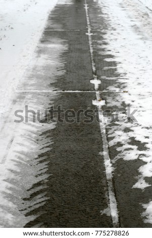 Wet road, pavement covered with beautiful and clean white snow. Autumn and winter holiday background