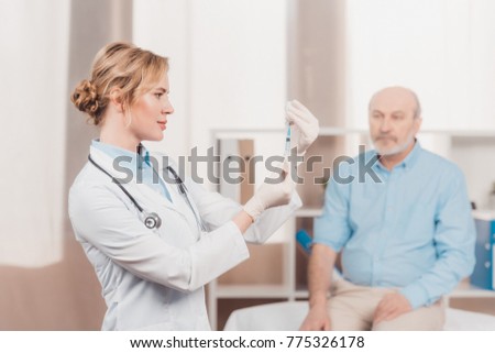 selective focus of doctor holding syringe for injection with senior patient behind in clinic