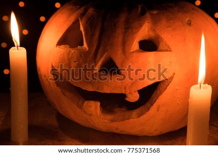 Orange pumpkin as a head with carved eyes and a smile with burning candles on a black background with a garland to the Halloween party
