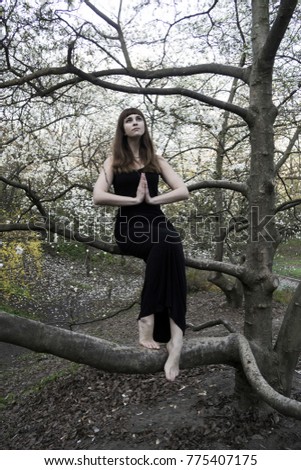 Brown haired young beautiful girl in charming black long dress in the garden with magnolia trees and flowers 
