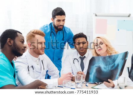 Multinational doctors examine the patient's x-ray. They consult each other. They look at the picture of the pelvis.