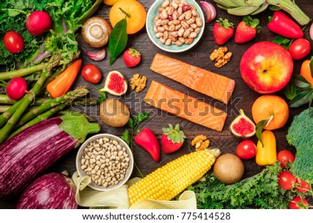 An overhead photo of fresh vegetables, fruits, legumes, and fish, healthy diet ingredients, shot from above on a dark rustic texture. Organic food or groceries shop banner