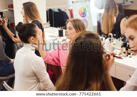 Three professional make-up artists work with beautiful young women. School of professional make-up
