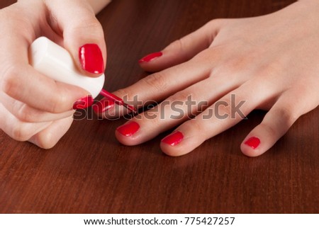 Woman applying red color nail polish on wooden table. Close up