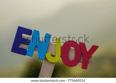word " enjoy " made by colorful wooden alphabet on blurred nature background.