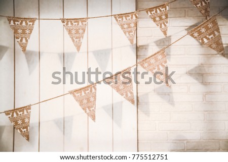 triangular flags on a rope in a Christmas theme with deer and snowflakes stretched against a white wall of wood and brick.