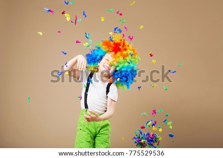Brazilian Carnival. Happy clown boy with large colorful wig. Let's party! Funny kid clown. 1 April Fool's day concept. Portrait of a child throws up a multi-colored tinsel and confetti. Birthday boy. Royalty-Free Stock Photo #775529536
