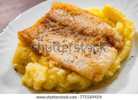 Fried fish fillet of cod with mashed potato in white plate on wooden background.