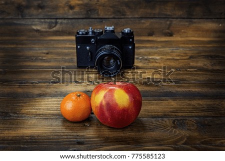 Film camera shoots mandarine and apple  on wooden background