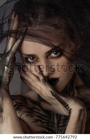 close up portrait of beautiful woman with smokey eyes. professional black and gold body painting. black hands. veil on face