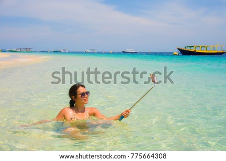 young beautiful and happy Asian Chinese woman having fun on sea water taking selfie picture with mobile phone camera on paradise beach water smiling in holiday and vacation concept
