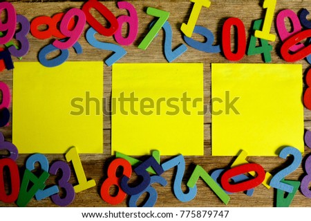 Education and business concept. Top view of three yellow empty sticky note on colorful wooden numbers. Copy space for text.
