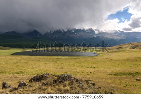 Scenic view with storm clouds over the plateau with a lake and mountains covered with snow and forest and part of a blue sky with sunlight