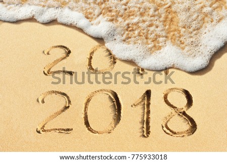  New Year is coming, concept - 2017 and 2018 handwritten in the sandy beach with soft ocean wave Royalty-Free Stock Photo #775933018