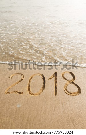  New Year concept -  2018 handwritten in the sandy beach with soft ocean wave