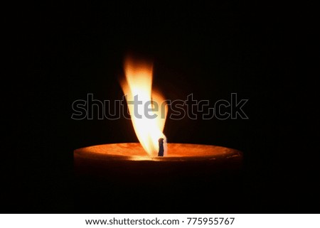 One Burning Candle Against Dark Background - Photograph of a burning candle with a dark background and the flame gently blowing in a wind. Selective focus on the candle wick.