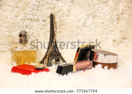 Cosmetics on white cloth with Eiffel Tower. Perfume of yellow color. Brilliant items. The chain winds on the tower.