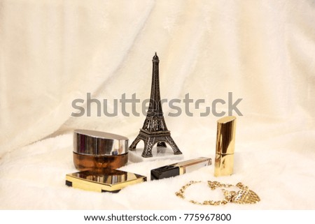 Cosmetics on white cloth with Eiffel Tower. Perfume of yellow color. Brilliant items. The chain winds on the tower.