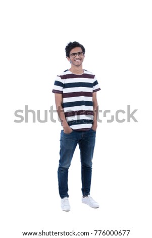 Full-length shot of handsome happy teenager with hands in pocket, he is wearing eyeglasses, striped t-shirt, jeans pants, and white sneakers. Isolated on white background.