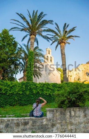 A girl photographer takes pictures of a church among green palms.