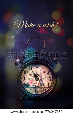 Close up of an old vintage watch with Eiffel tower print, with the message Make a wish for New Years Eve, with sparkles and colorful bokeh on a black background