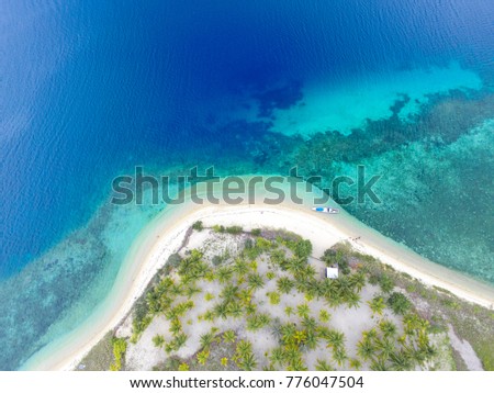 Private island. Top view of small isolated tropical island with white sandy beach and blue transparent water and coral reefs